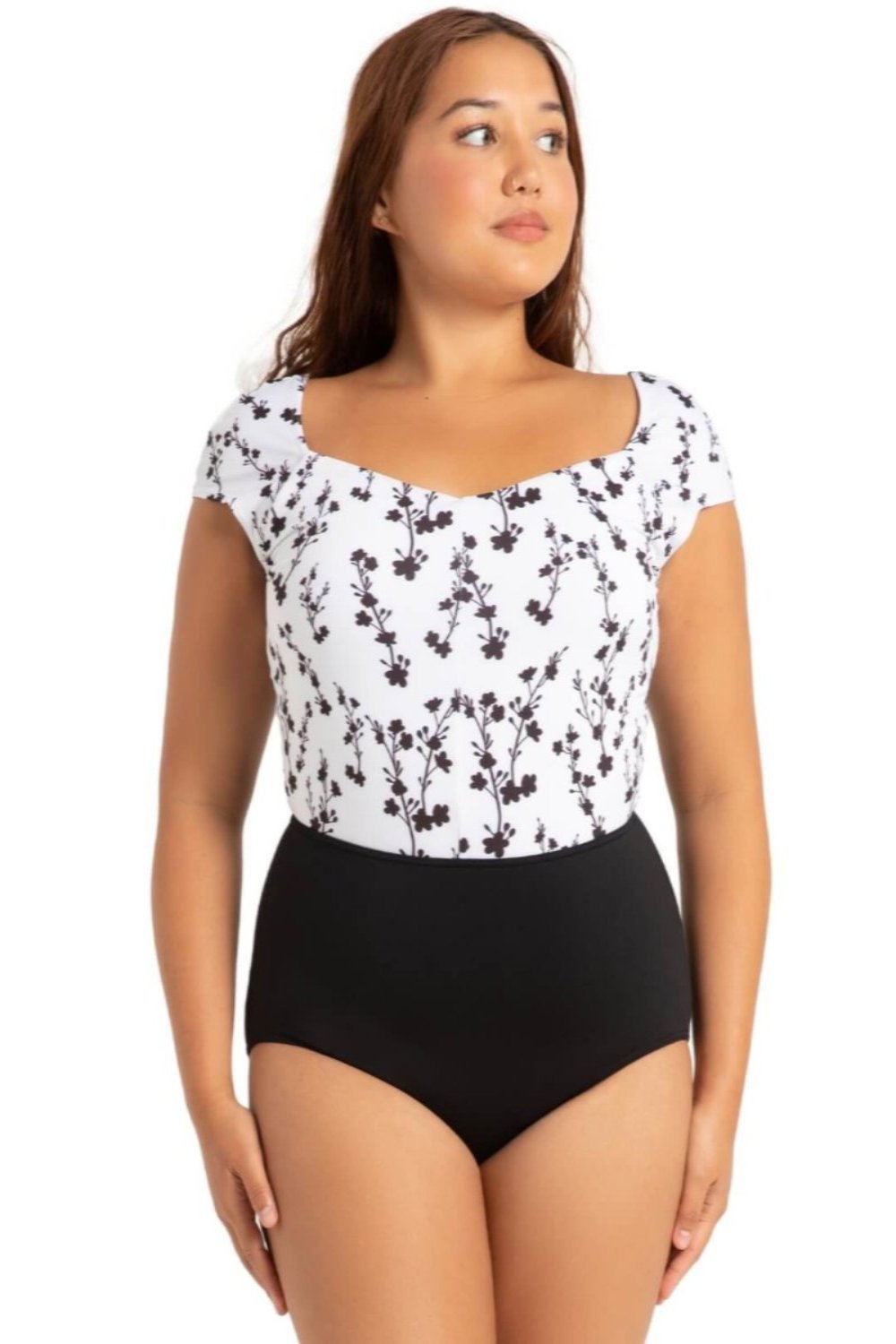 pretty young woman with dark hair and sun tan wearing cap sleeved leotard in white fabric with black floral print 